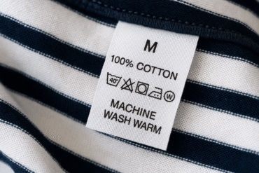 نمای نزدیک از لیبل مراقبت روی تی‌شرت راه‌راه؛ آیکون‌های شست‌وشو، بلیچ، خشک‌کن، اتو و خشک‌شویی دیده می‌شود.